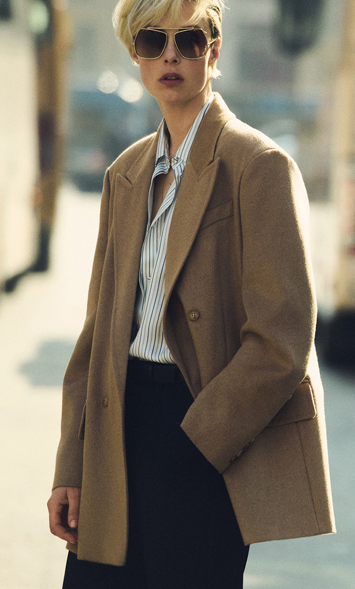 Model in double-breasted blazer-style Max Mara Olimpia Jacket in camel colour, with dark glasses and shirt in an urban environment.